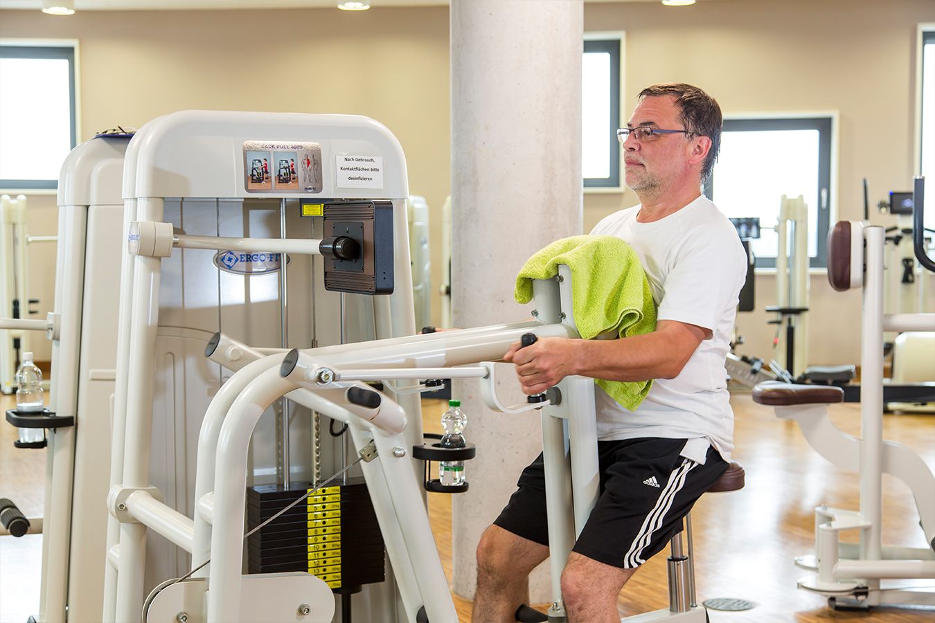 Mann mit grünem Handtuch trainiert an Gerät