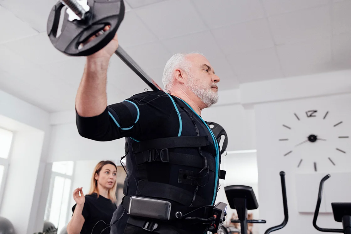 Älterer Mann mit EMS Anzug beim Hanteltraining