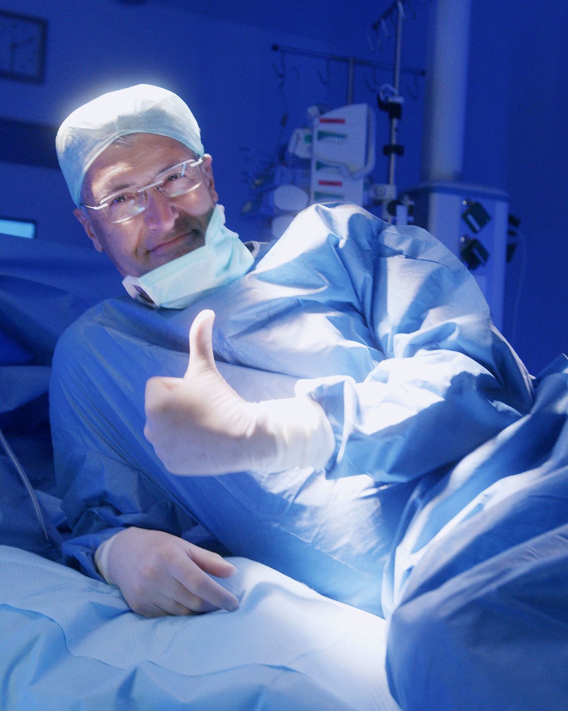 Chirurg liegt auf OP-Tisch und zeigt Daumen hoch
