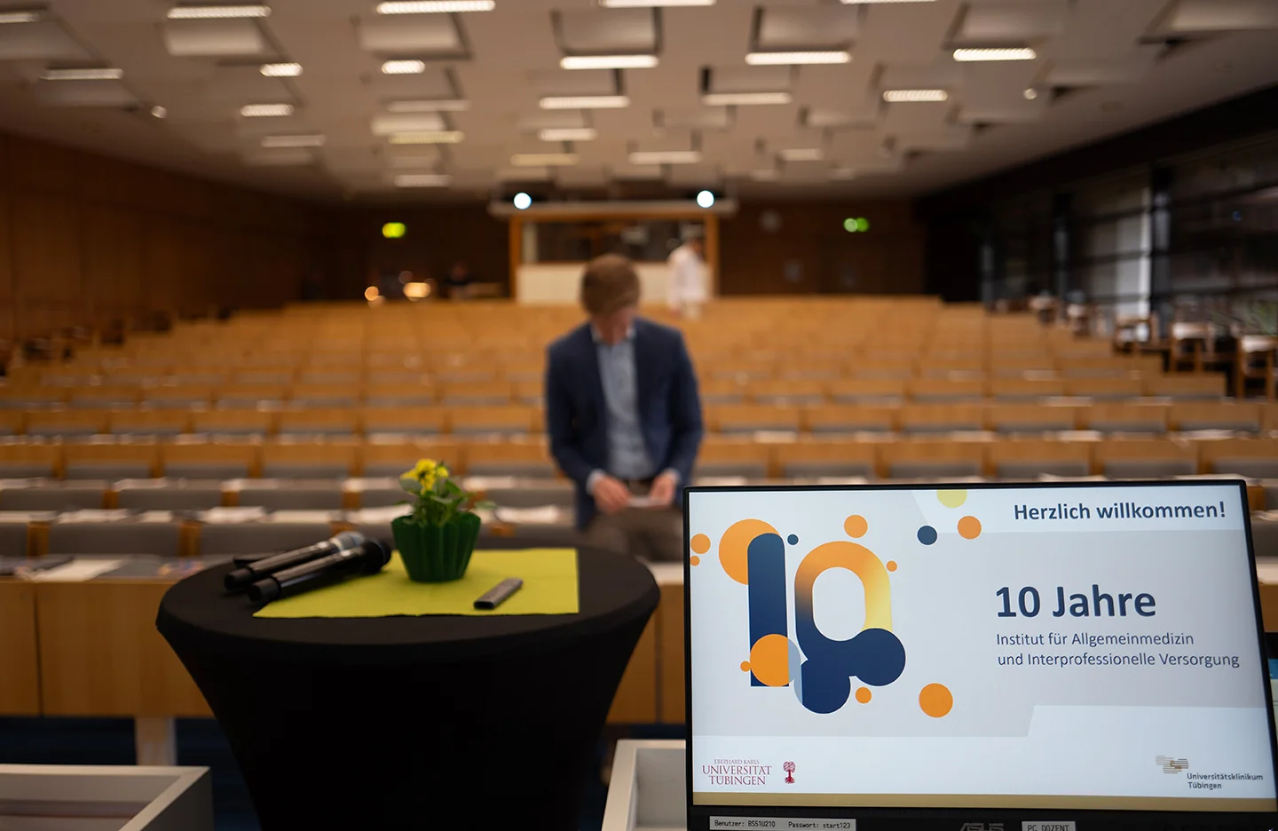 Hörsaal Jubiläumsveranstaltung mit Bildschirm im Vordergrund und Startfolie zum Jubiläum