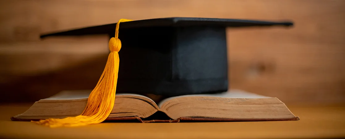 Schmuckbild: Graduierungskappe auf Buch und Holzhintergrund