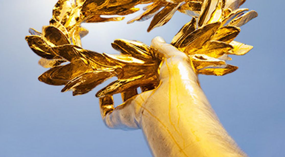 Goldene Hand mit Lorbeerkranz reckt sich in den blauen Himmel