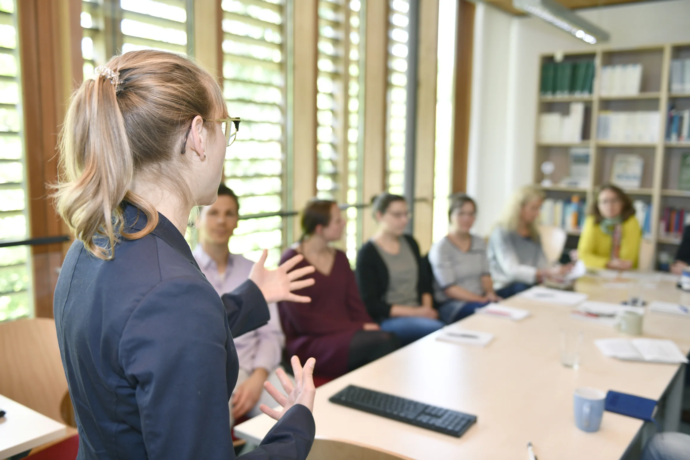 Frau referiert vor einer sitzenden Gruppe.