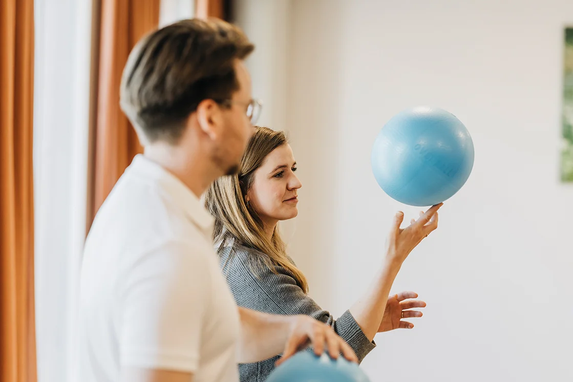 zwei Personen halten jeweils einen Ball in der Hand, eine Raum balanciert ihren Ball auf einem Finger, der nebenstehende Mann hält seinen Ball mit beiden Händen fest.