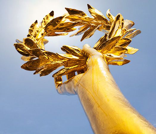 Goldene Hand mit Lorbeerkranz reckt sich in den blauen Himmel