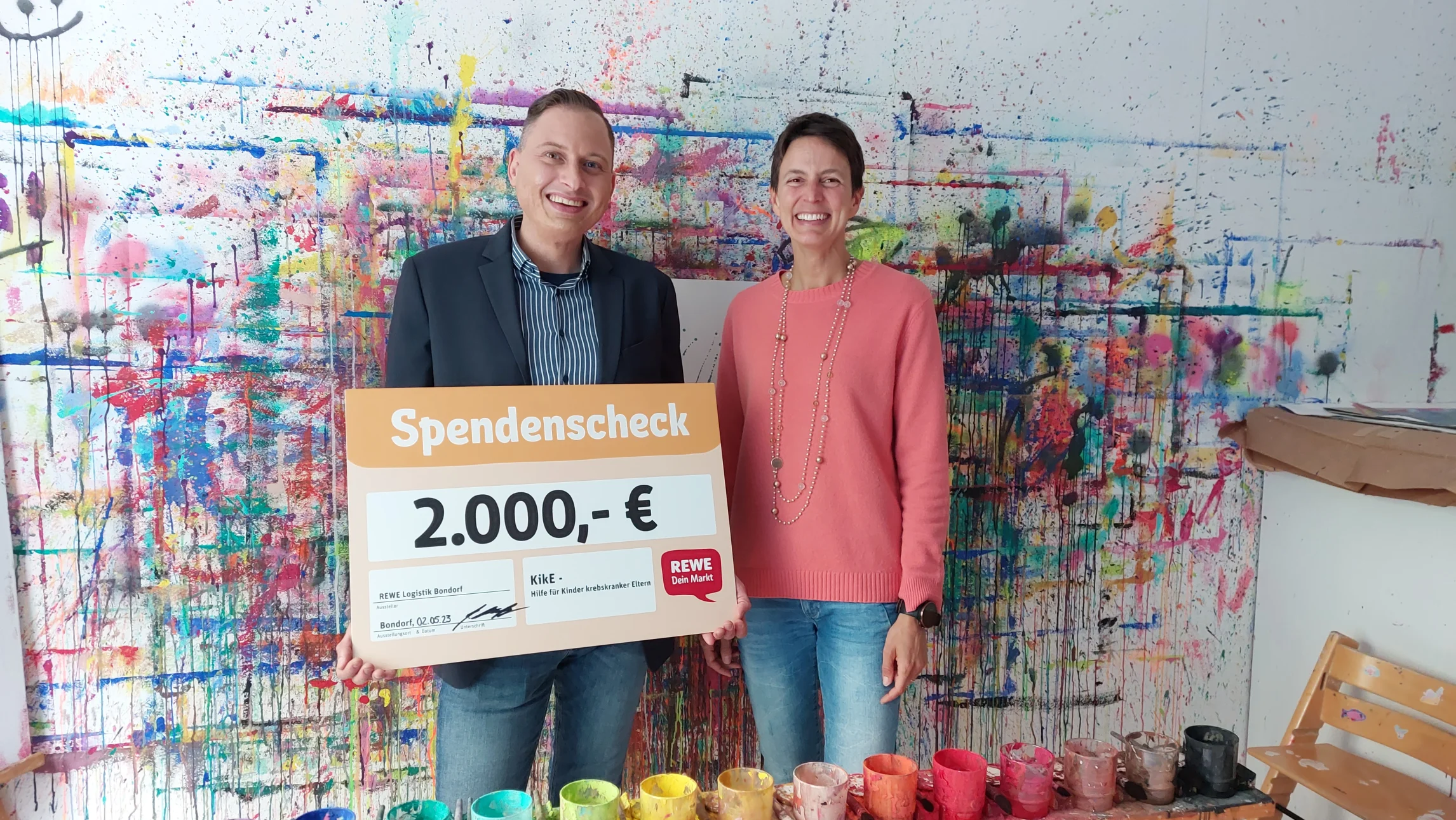 Bild der Spendenübergabe vor bunter Wand