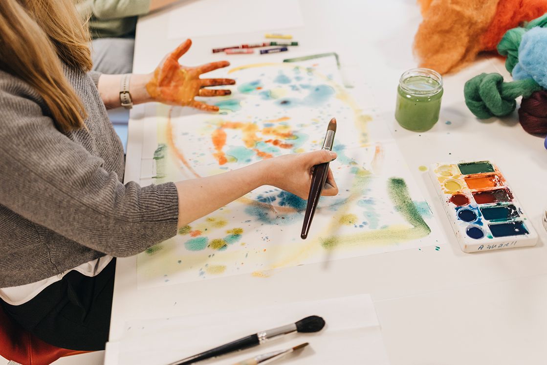 Patientin bei einer kunsttherapeutsichen Einheit in der psychosomatischen Einrichtung, malt mit Wasserfarben auf großem Papierbogen