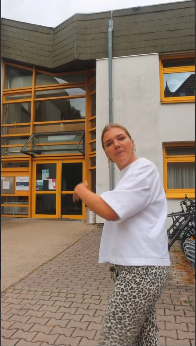 Junge Frau vor dem KJP Gebäude macht eine einladende Geste