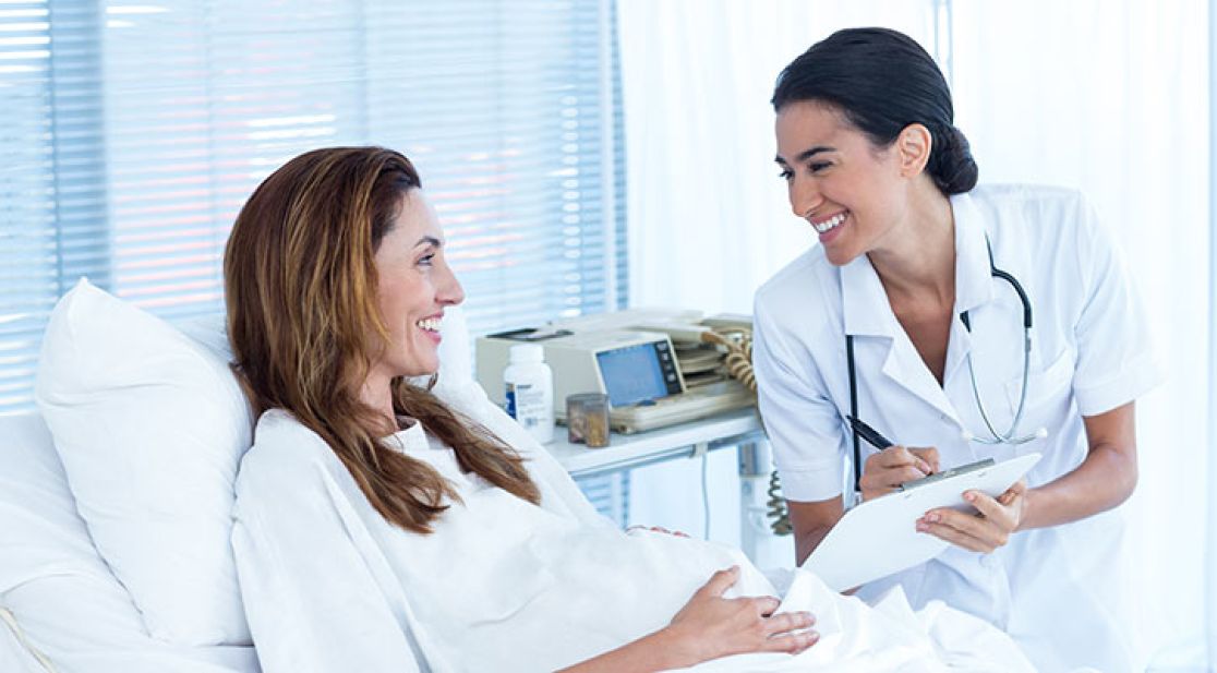 Frau liegt in einem Bett und wird von Krankenschwester befragt