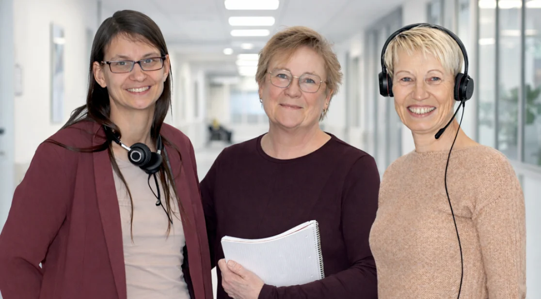 Die drei Krebswegweiserinnen blicken in die Kamera vor einem Krankenhaushintergrund (Hintergrund mit KI generiert)