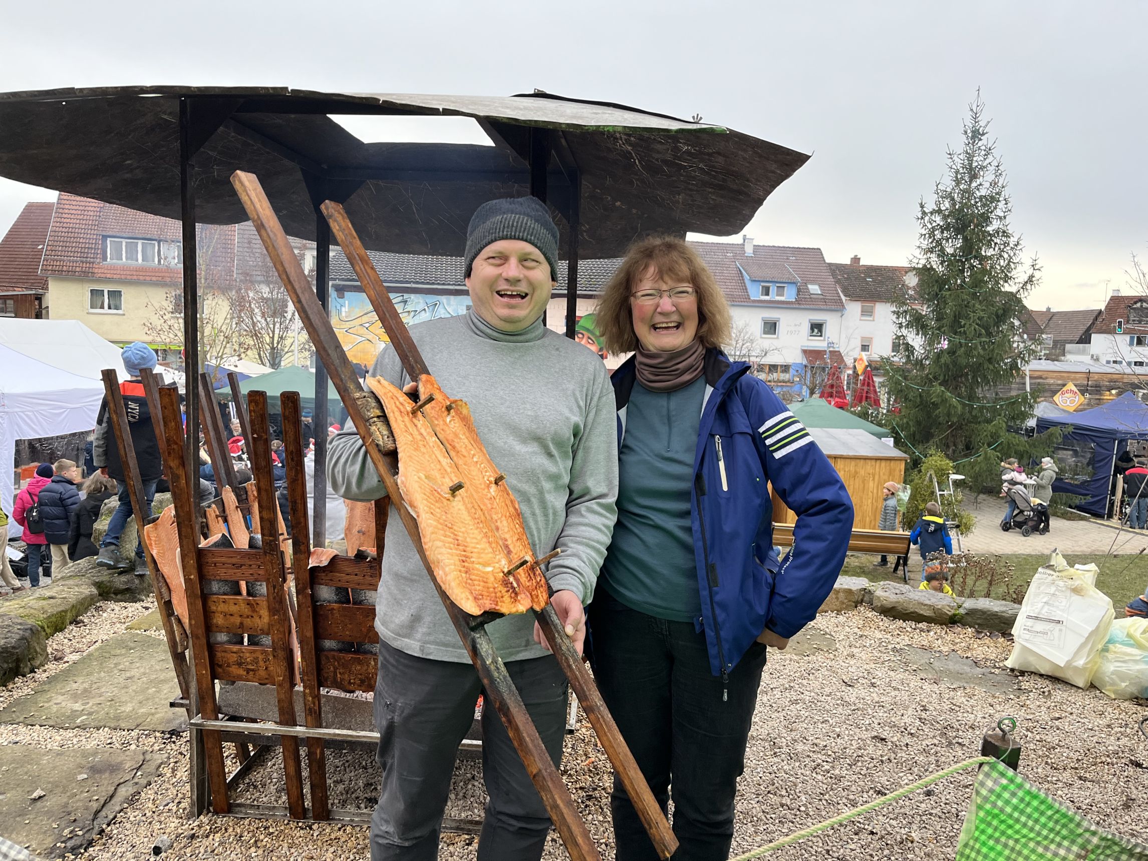 Zwei Personen halten Flammlachs vor dem Verkaufsstand