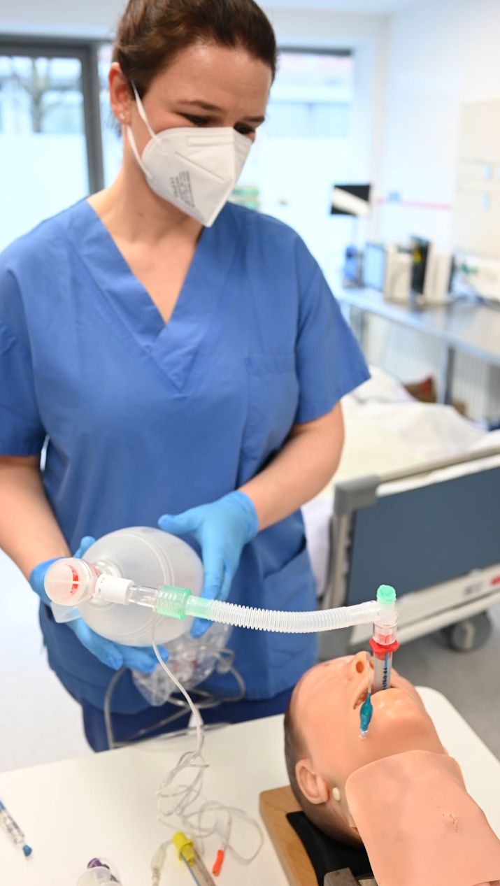 Pflegerin mit Mundschutz beatmet die Reanimationspuppe