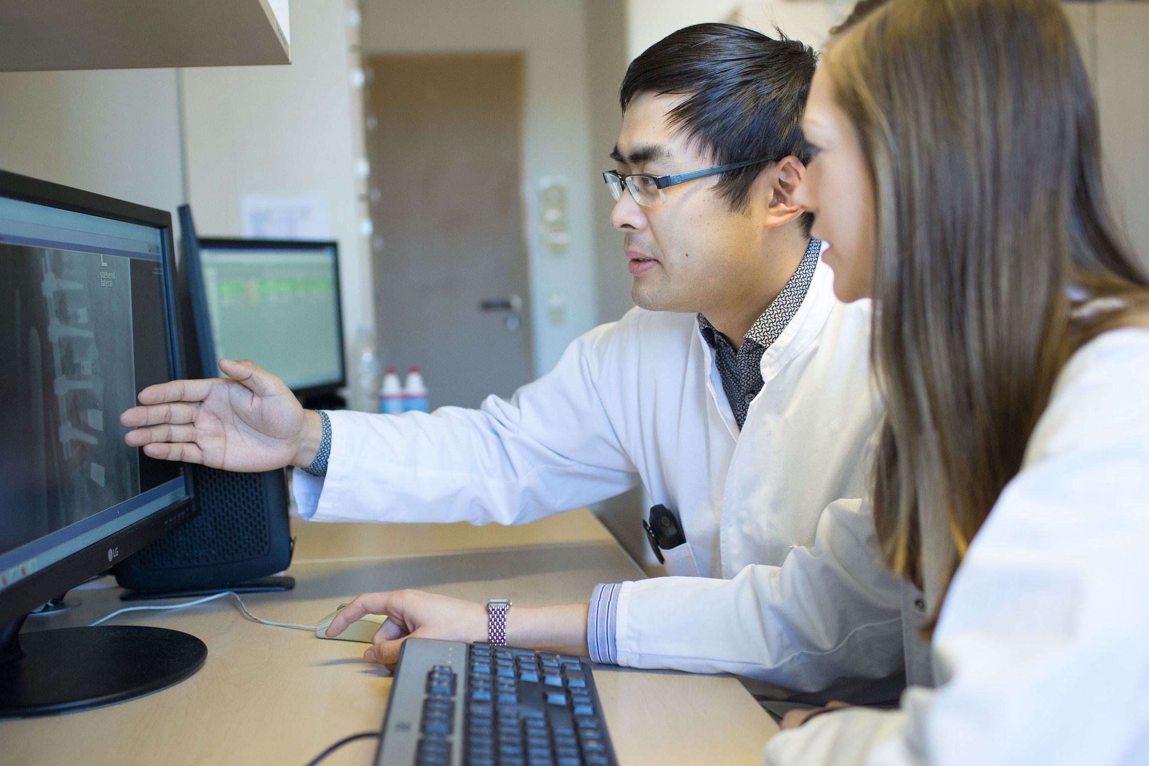 Zwei Ärzte besprechen sich vor dem PC mit Aufnahmen einer Wirbelsäule