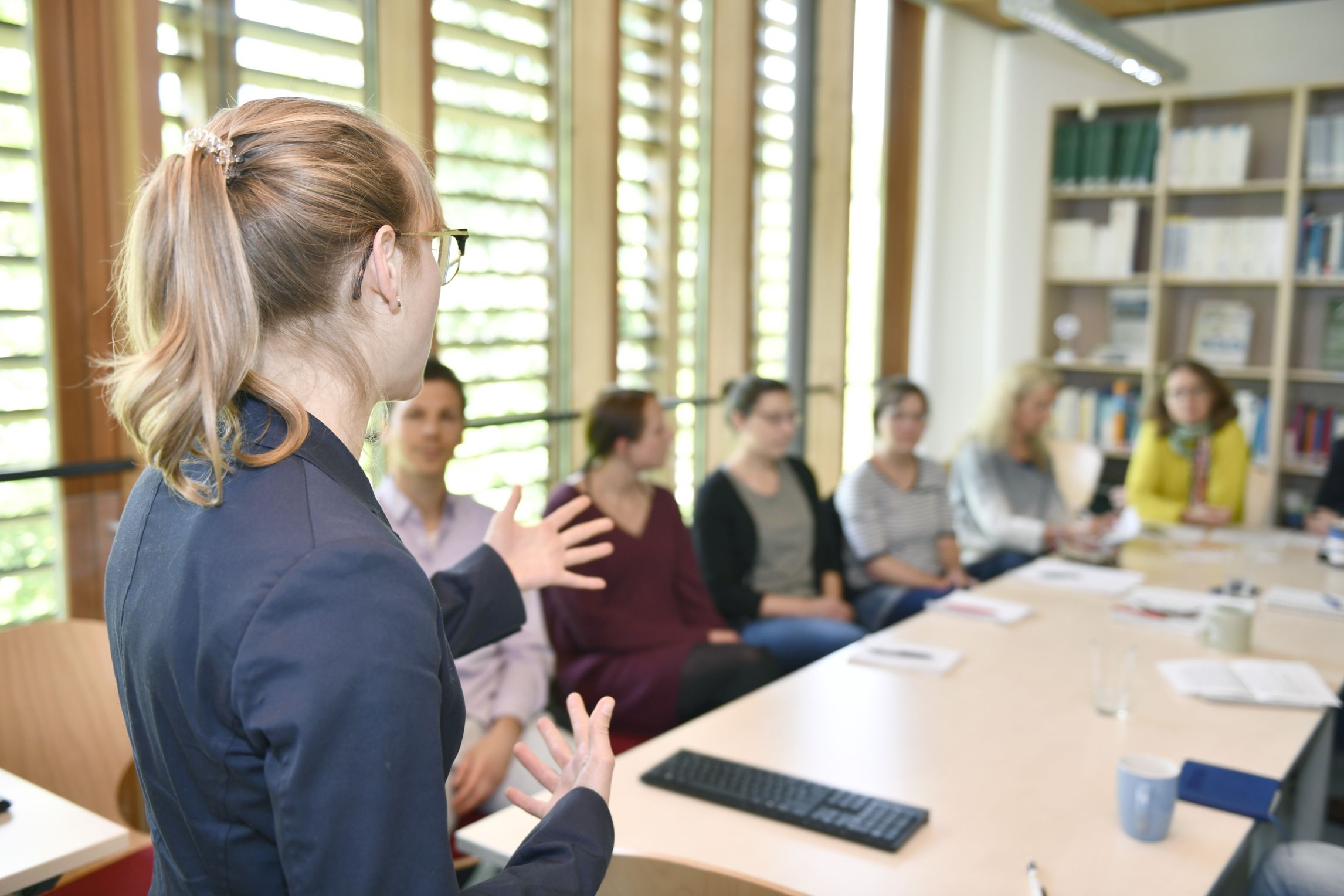 Frau referiert vor einer sitzenden Gruppe.