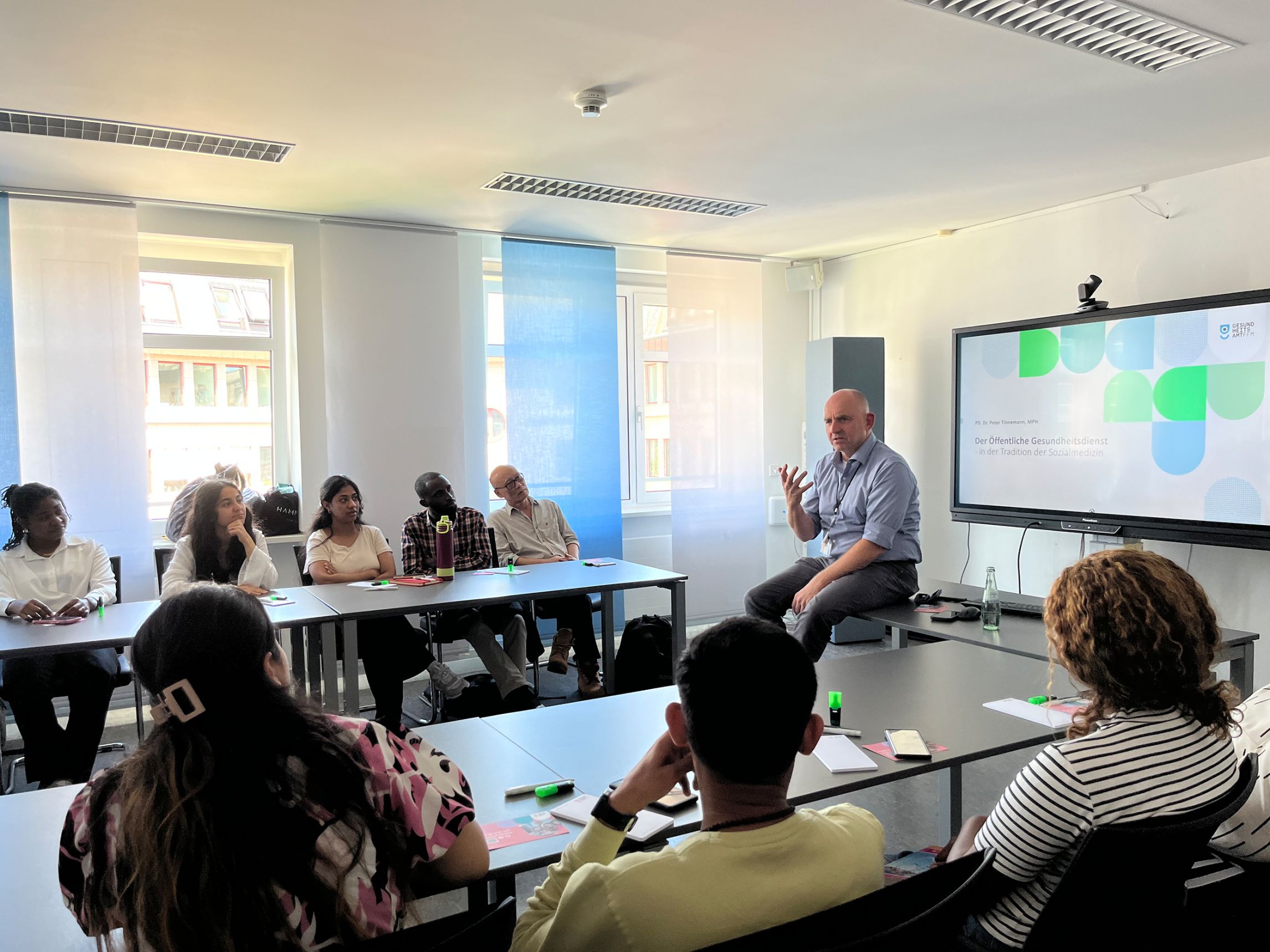 Studierende hören bei einem Vortrag zu und sitzen an Tischen