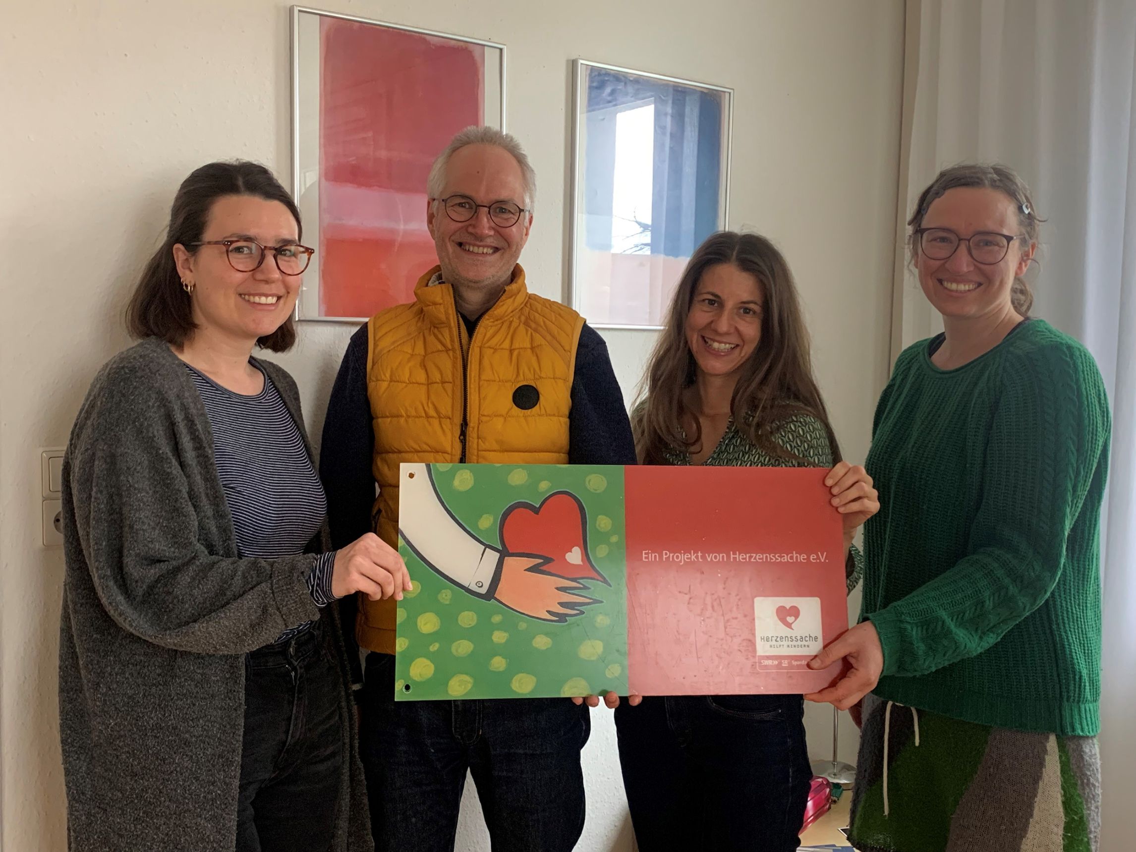 Vier Personen bei der Spendenübergabe halten den symbolischen Spendenscheck