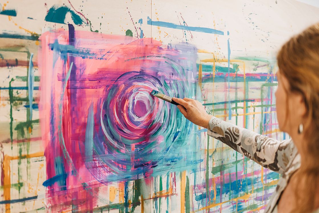 Frau malt mit bunten Farben mit einem Pinsel eine kreisförmige Form auf ein großes Wandplakat
