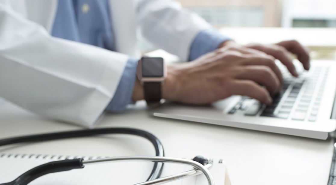 Hände tippen auf Tastatur, Stethoskop im Vordergrund