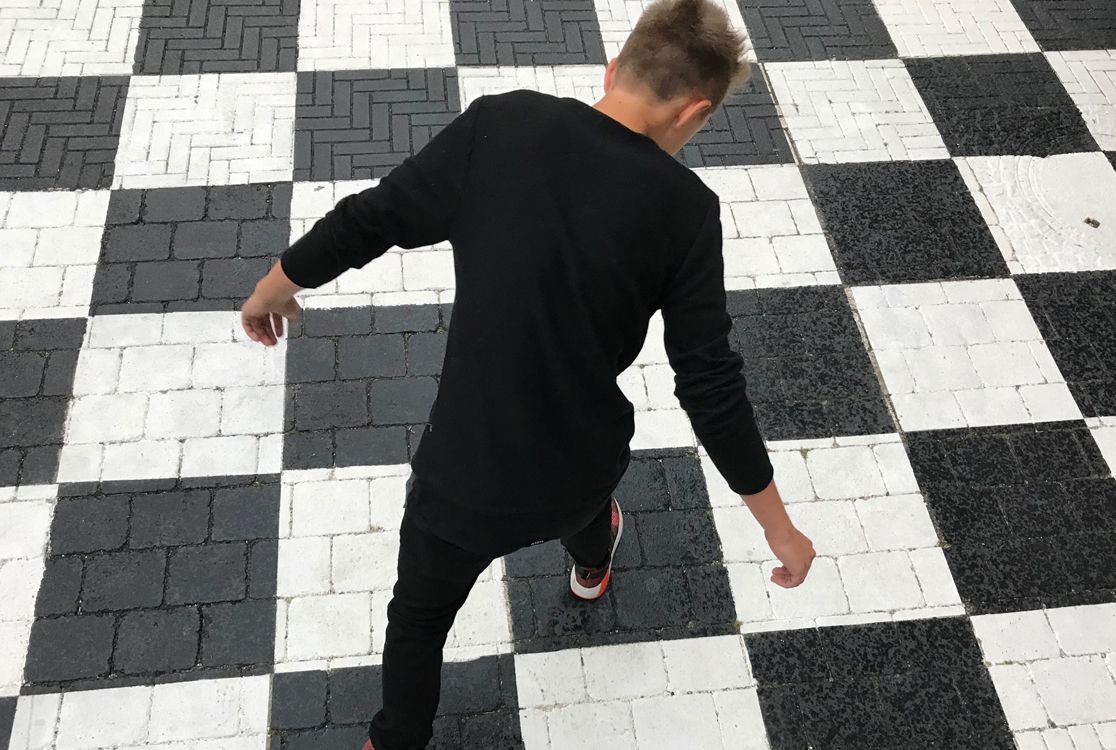 Junge hüpft auf schwarz-weiss kariertem Untergrund