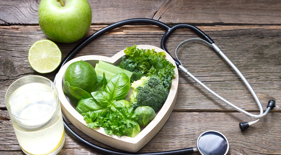 Herz mit grünem Gemüse gefüllt mit Sthetoskop und blauen Hanteln und Turnschuhen