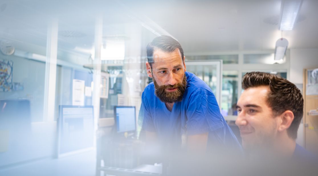 Zwei männliche Pflegekräfte im Gespräch, verschwommener Vordergrund