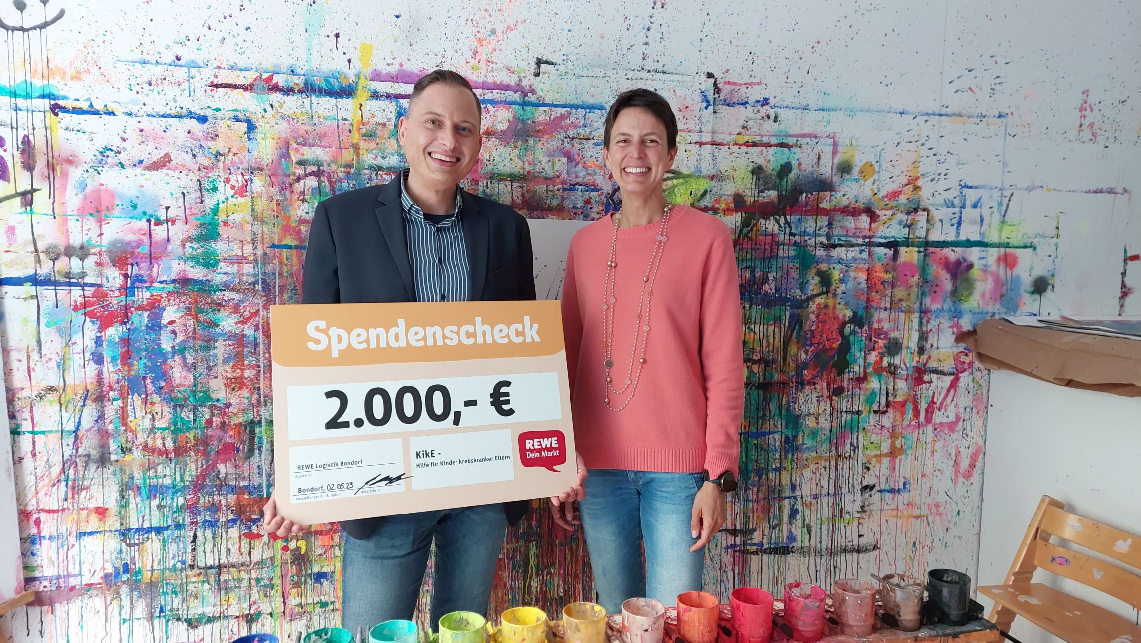 Bild der Spendenübergabe vor bunter Wand