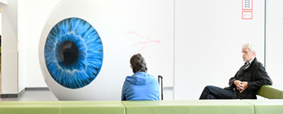 Grüne Bänke im Wartebereich der Augenklinik, im Hintergrund das Augenmodell