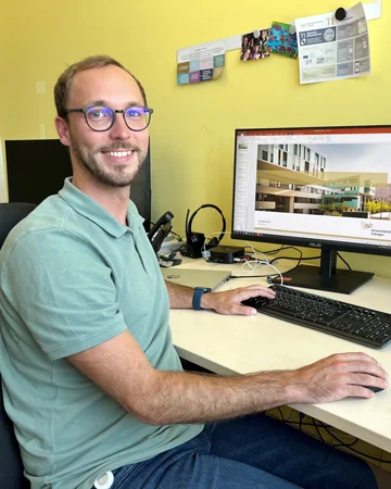 Jan Baumann sitzt vor dem Computer im gelben Büro