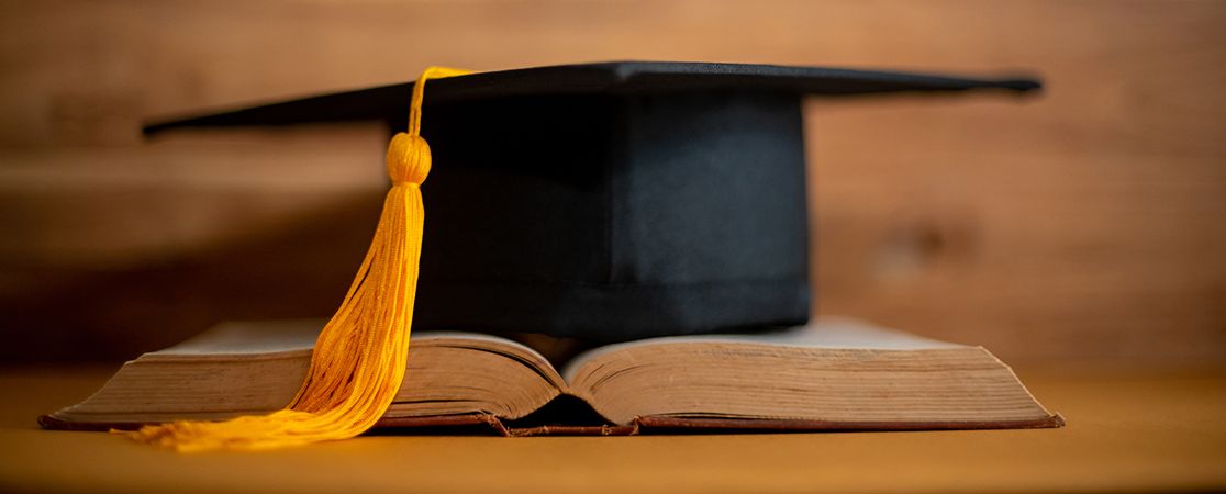 Decorative picture: graduation cap on book and wooden background