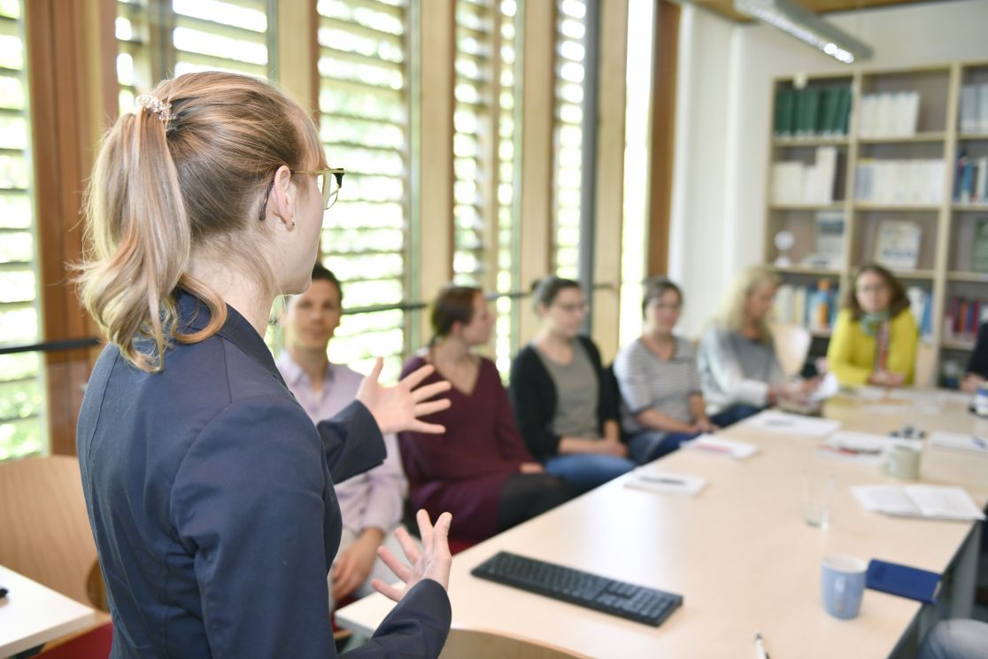 Frau referiert vor einer sitzenden Gruppe.