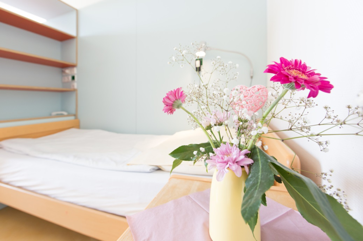 Stationszimmer mit Bett im Hintergrund und Tisch mit Blumen