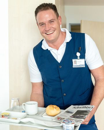 Michael Egeler serviert ein Tablett mit Zeitung und Frühbgstück