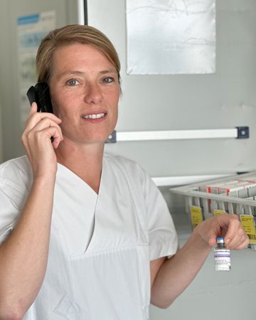 Tina Hansmann telefoniert und hält ein Fläschchen mit Impfstoff