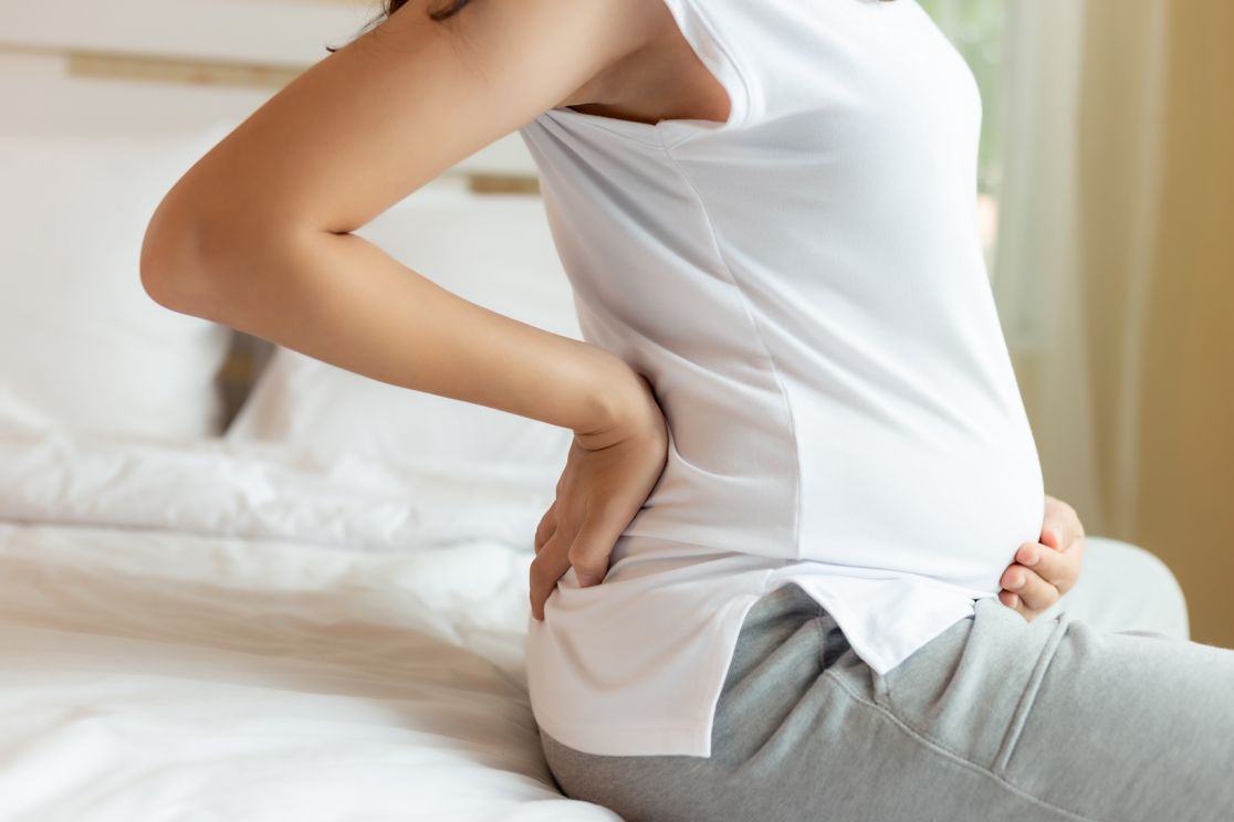 Schwangere mit Rückenschmerzen sitzt auf Bett